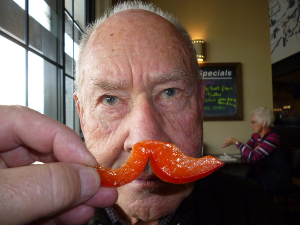 An older gentleman holding a pepper up to his face to portray a moustache