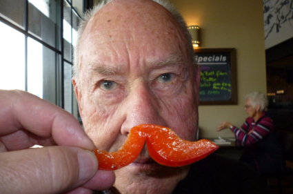 An older gentleman holding a pepper up to his face to portray a moustache