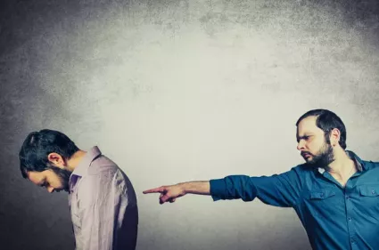A man pointing at another man whose back is turned and head is down
